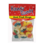 A clear bag labeled Handy Candy ASST FRUIT RINGS contains colorful sugar-coated gummy rings in red, yellow, orange, blue, and green. The package features a red and yellow label decorated with stars.